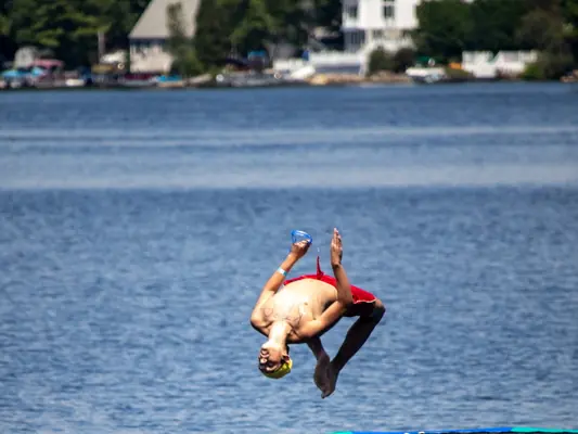 A camper mid-backflip off the water trampoline