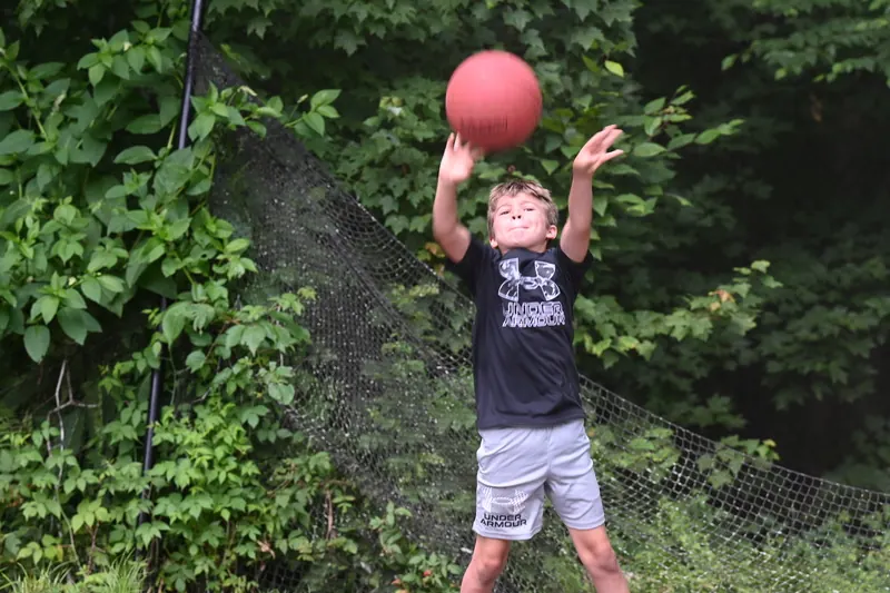 A camper catches a red ball by the net at the edge of the woods
